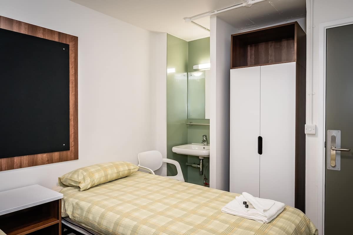 Une petite chambre à coucher, bien rangée, avec un lit, une table de chevet et une armoire.