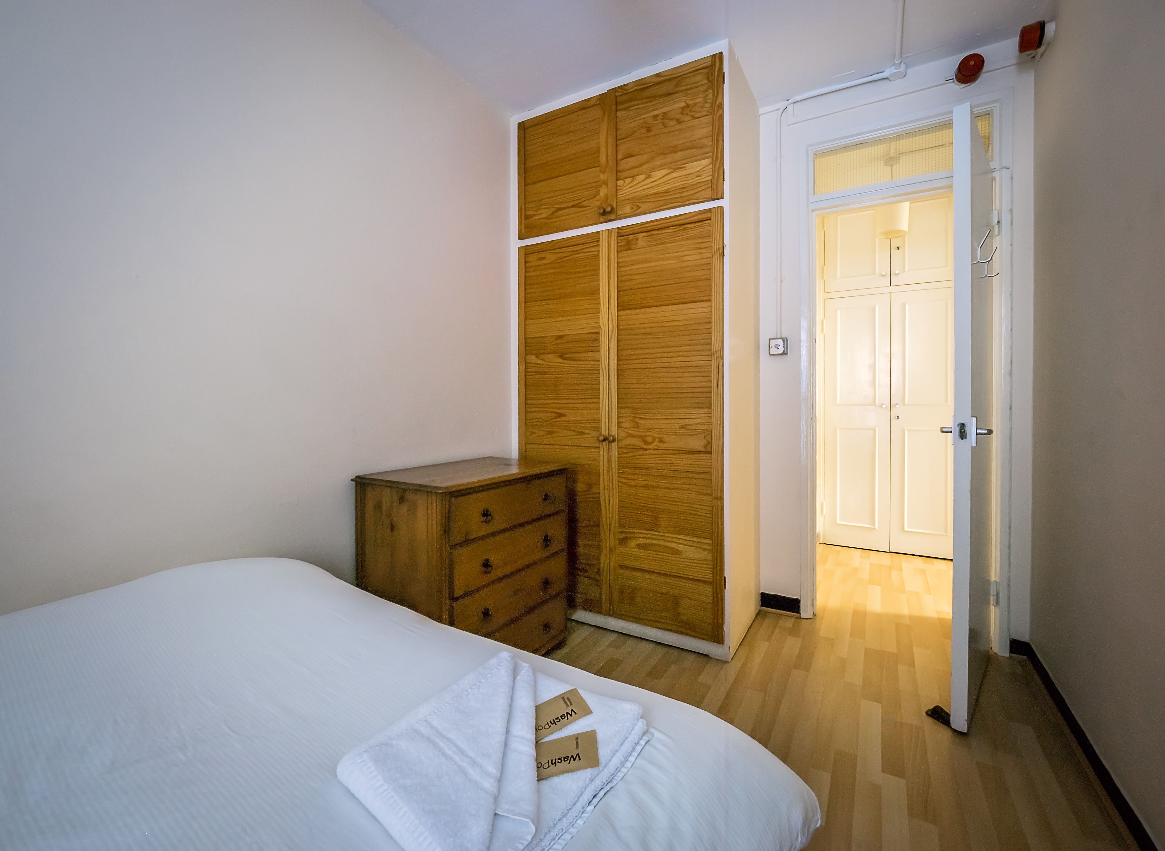 A bedroom with a bed, wooden wardrobe, and a door leading to another room.