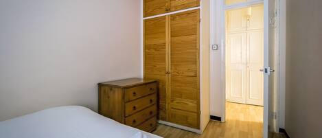 A bedroom with a bed, wooden wardrobe, and a door leading to another room.