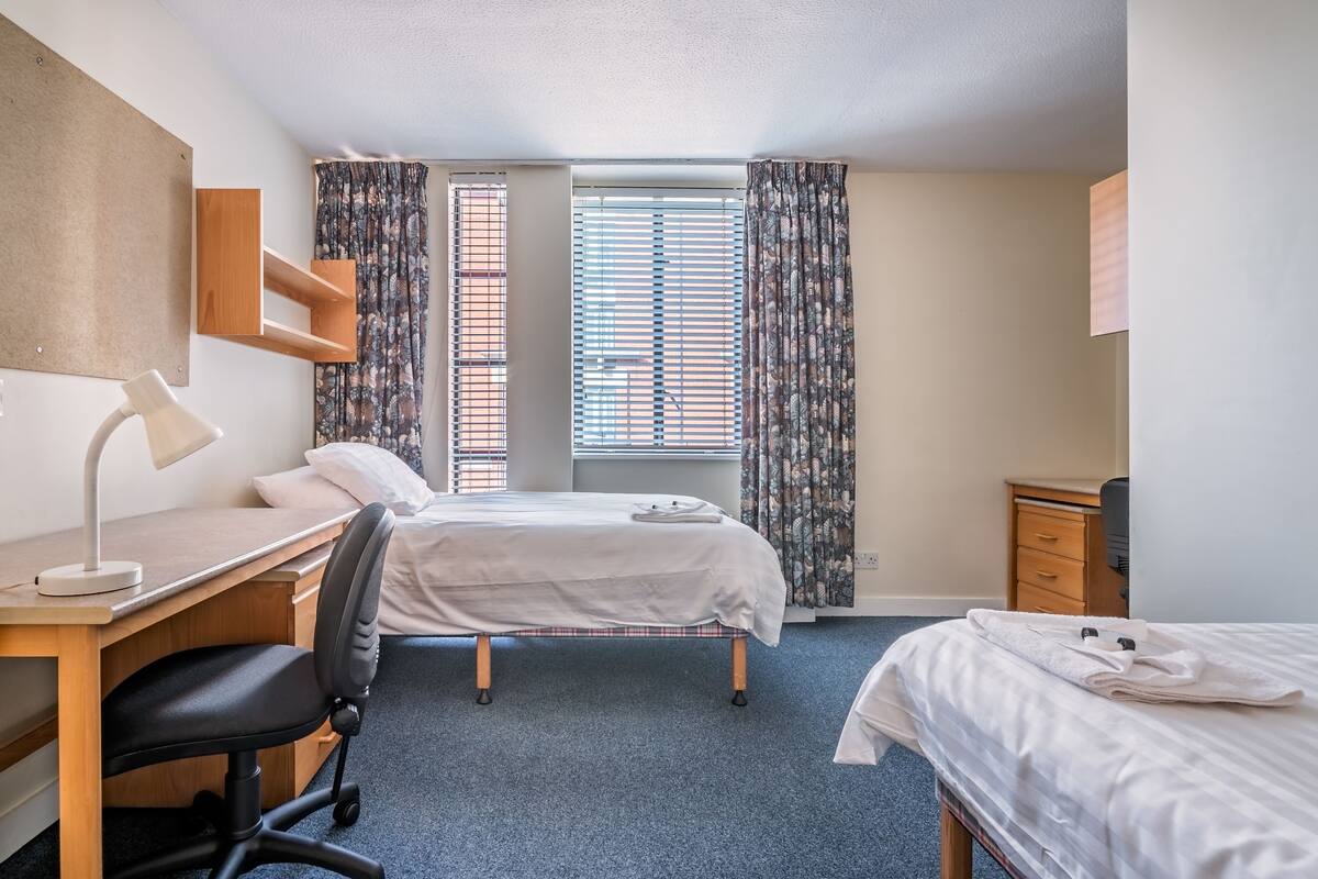 Une chambre d’hôtel avec un lit, un bureau, une chaise et une fenêtre avec des rideaux.