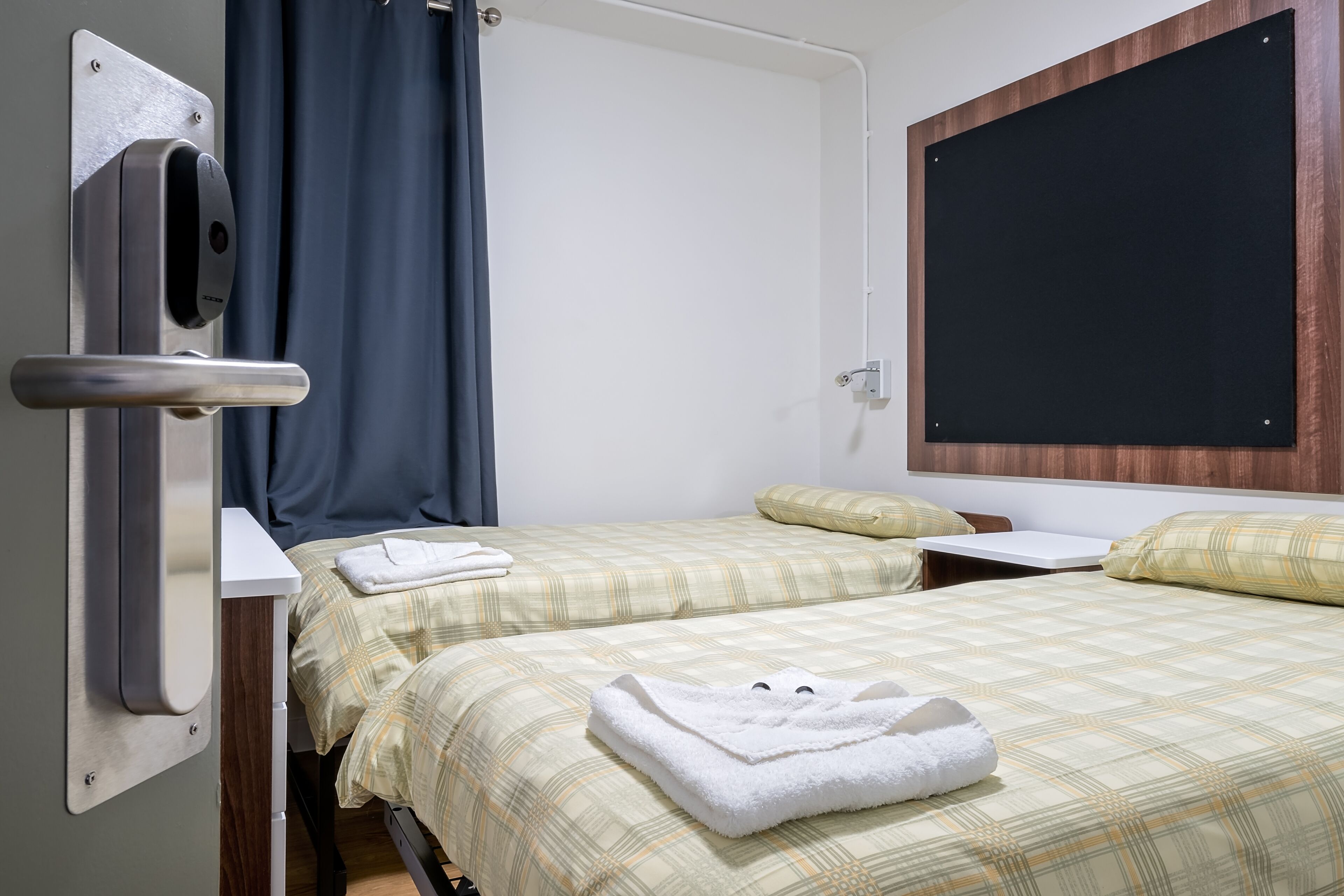Une chambre d’hôtel avec deux lits, un bureau, un tableau noir et un distributeur de serviettes.