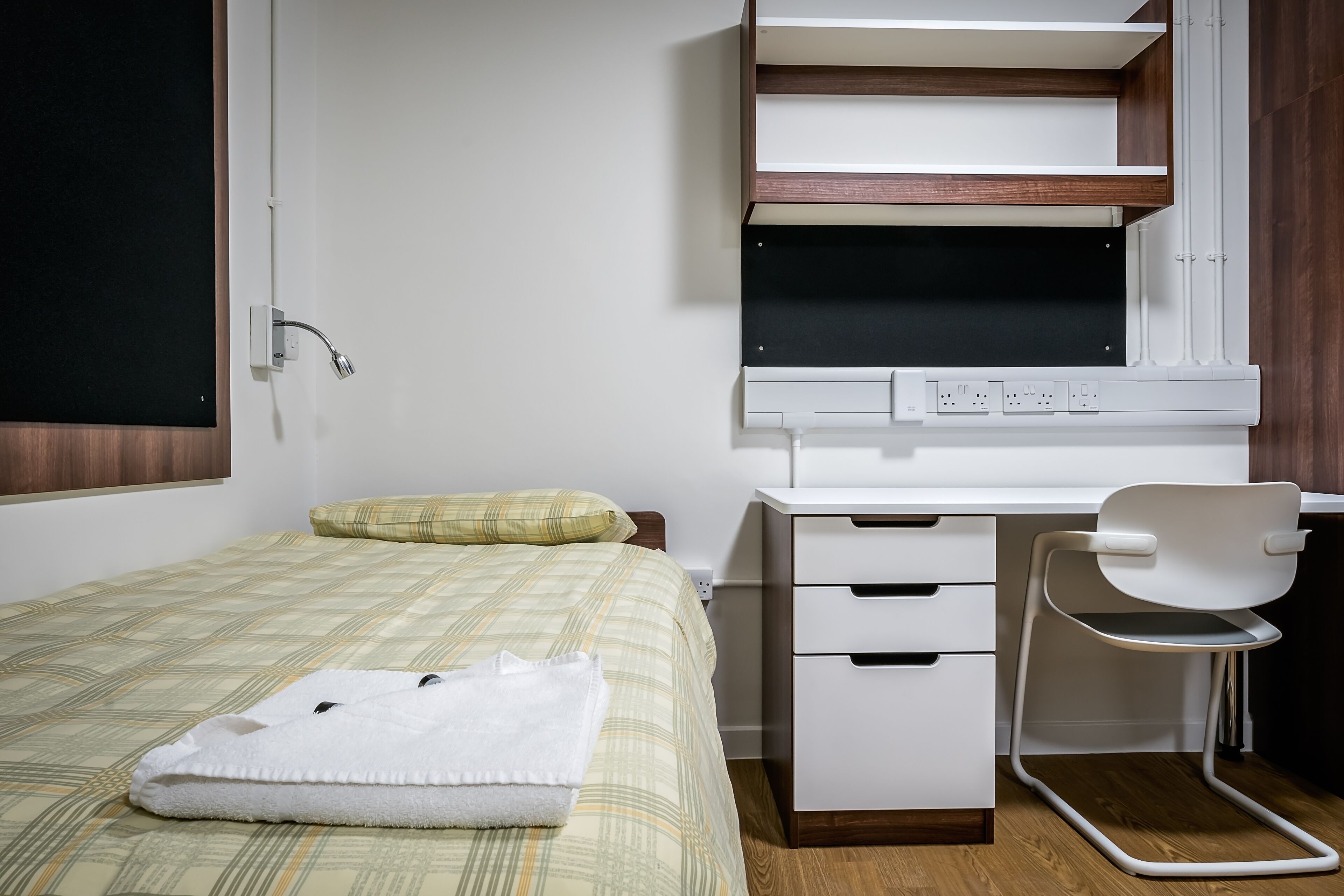 A bedroom with a bed, a desk, a chair, and a window.