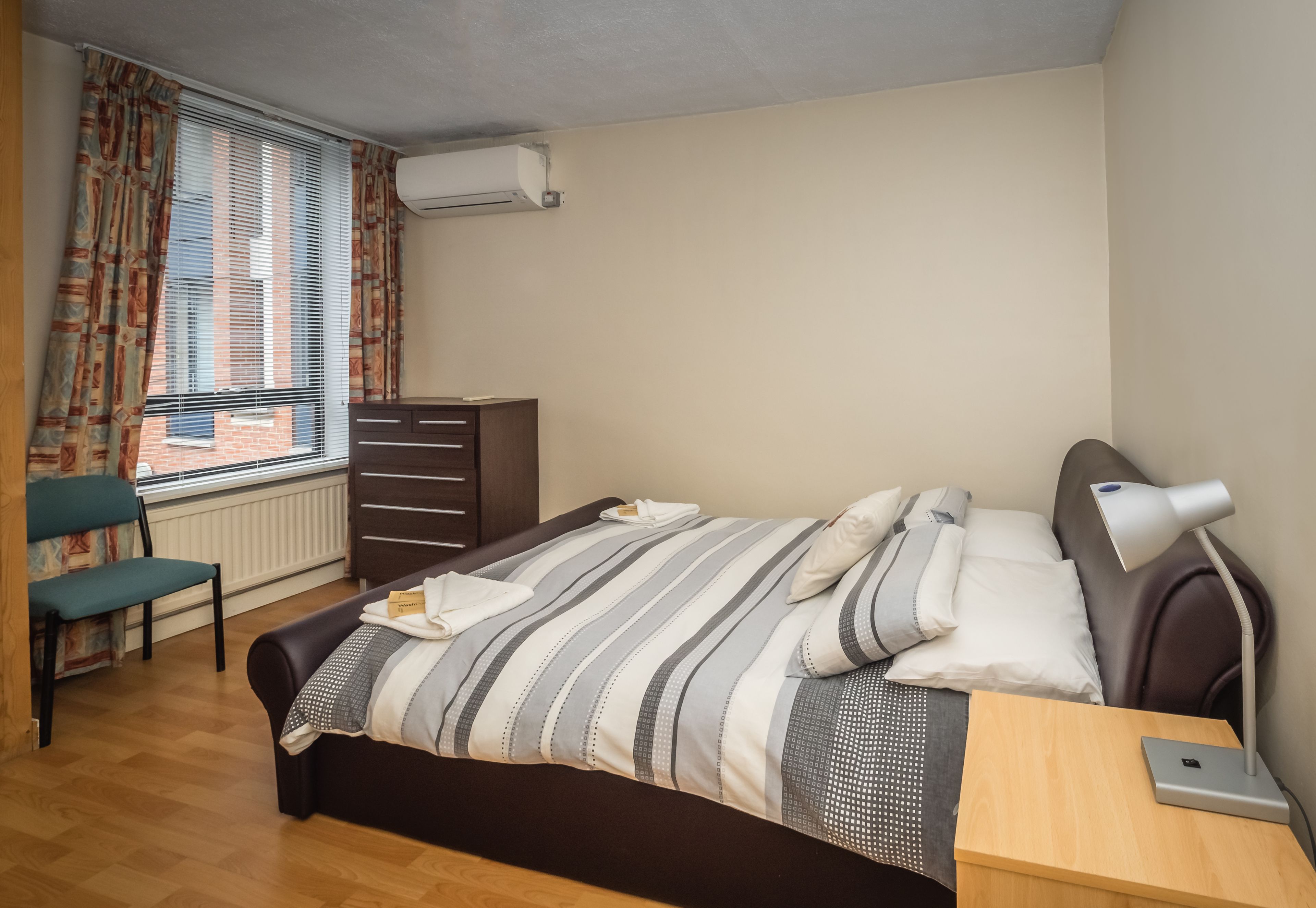 A neatly arranged bedroom with a bed, bedside table, lamp, and a chair.