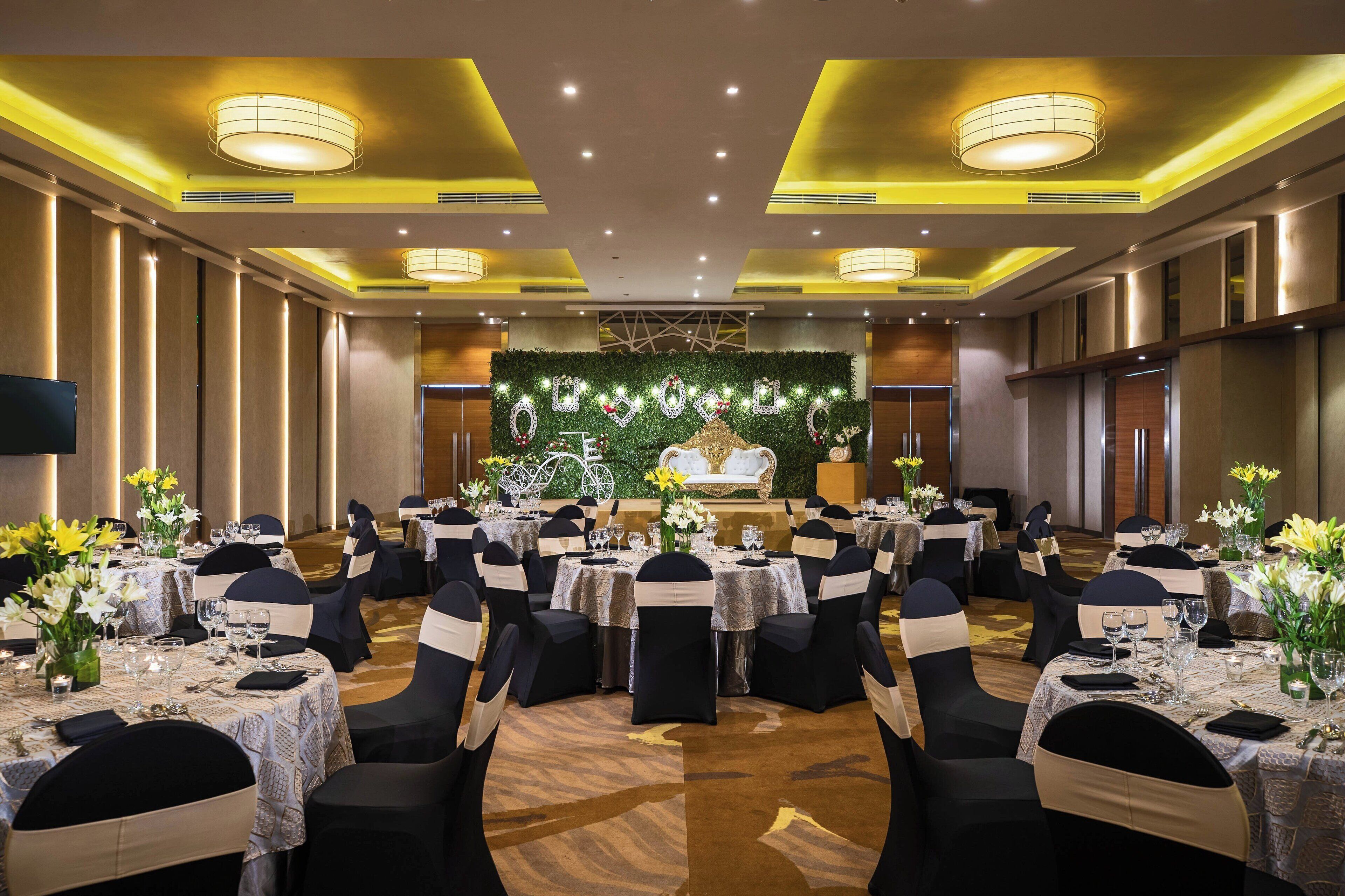 A banquet hall with round tables, black chairs, and yellow accents on the ceiling.