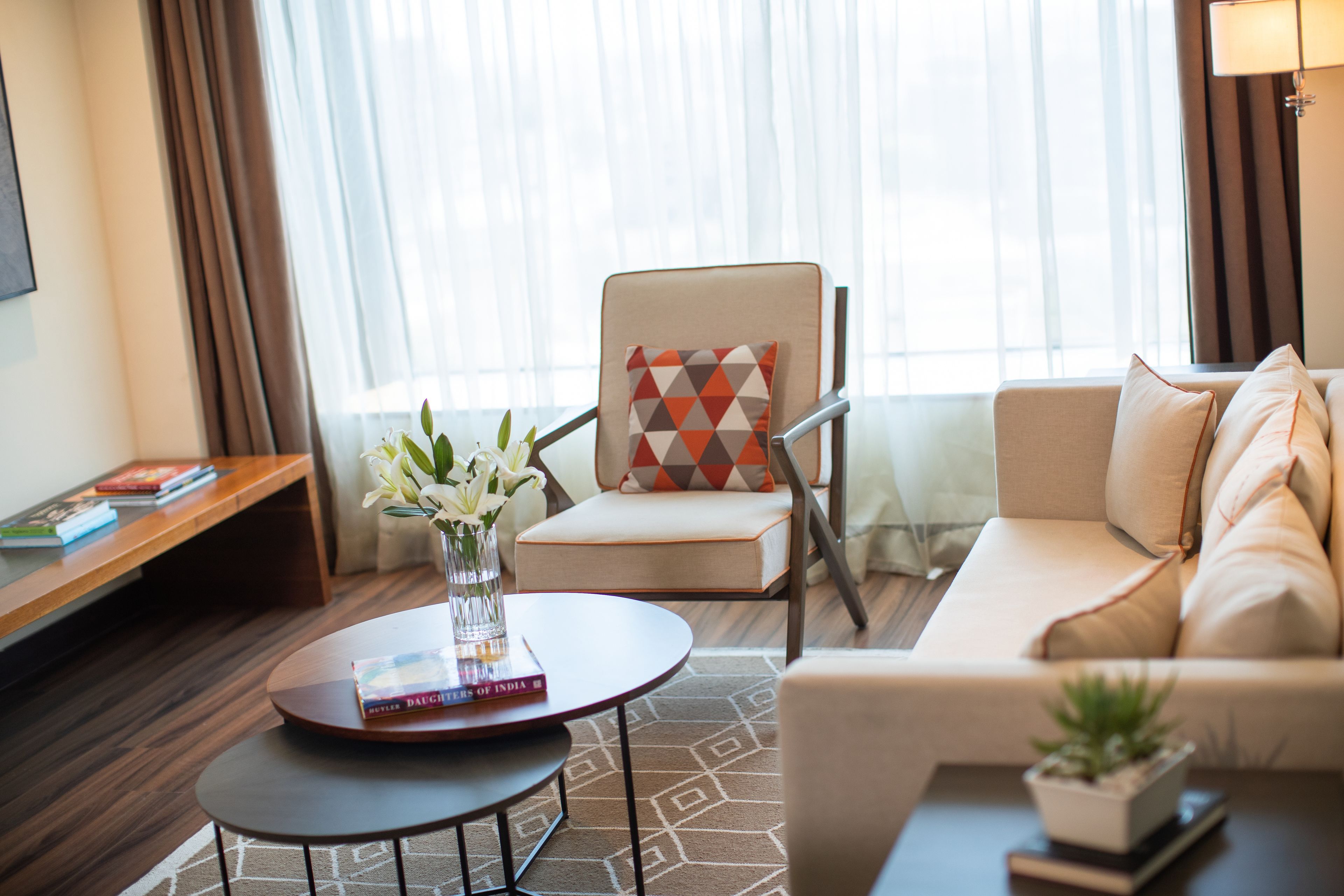 A modern hotel room with a sofa, armchair, and a small table with a vase of flowers.
