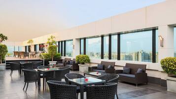 Una terraza en la azotea con mobiliario exterior, incluyendo mesas y sillas, y amplias ventanas que ofrecen vistas a la ciudad.