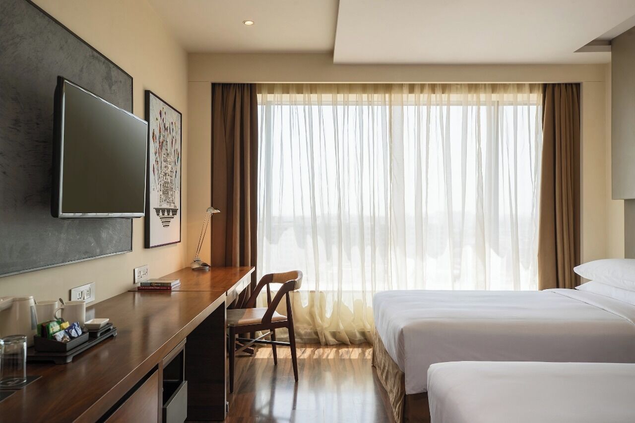 Une chambre d’hôtel avec un lit, un bureau, une chaise, une télévision et une fenêtre avec des rideaux.