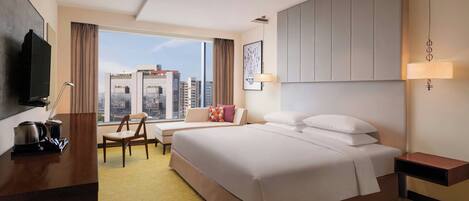 A hotel room with a large bed, a desk with a flat-screen TV, a chair, and a sofa.