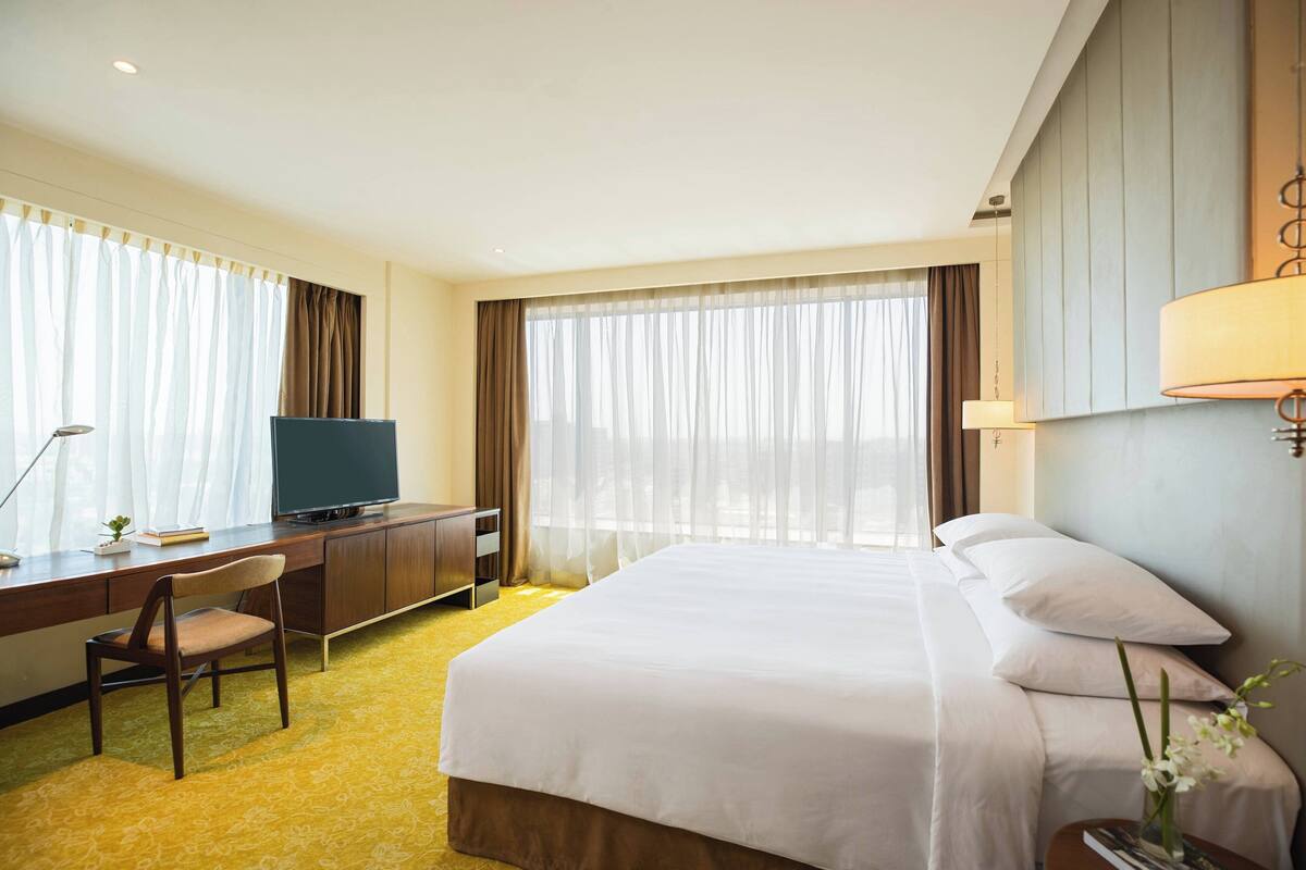 Una habitación de hotel con cama, escritorio con televisor, silla y lámpara.