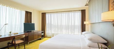 Una habitación de hotel con cama, escritorio con televisor, silla y lámpara.