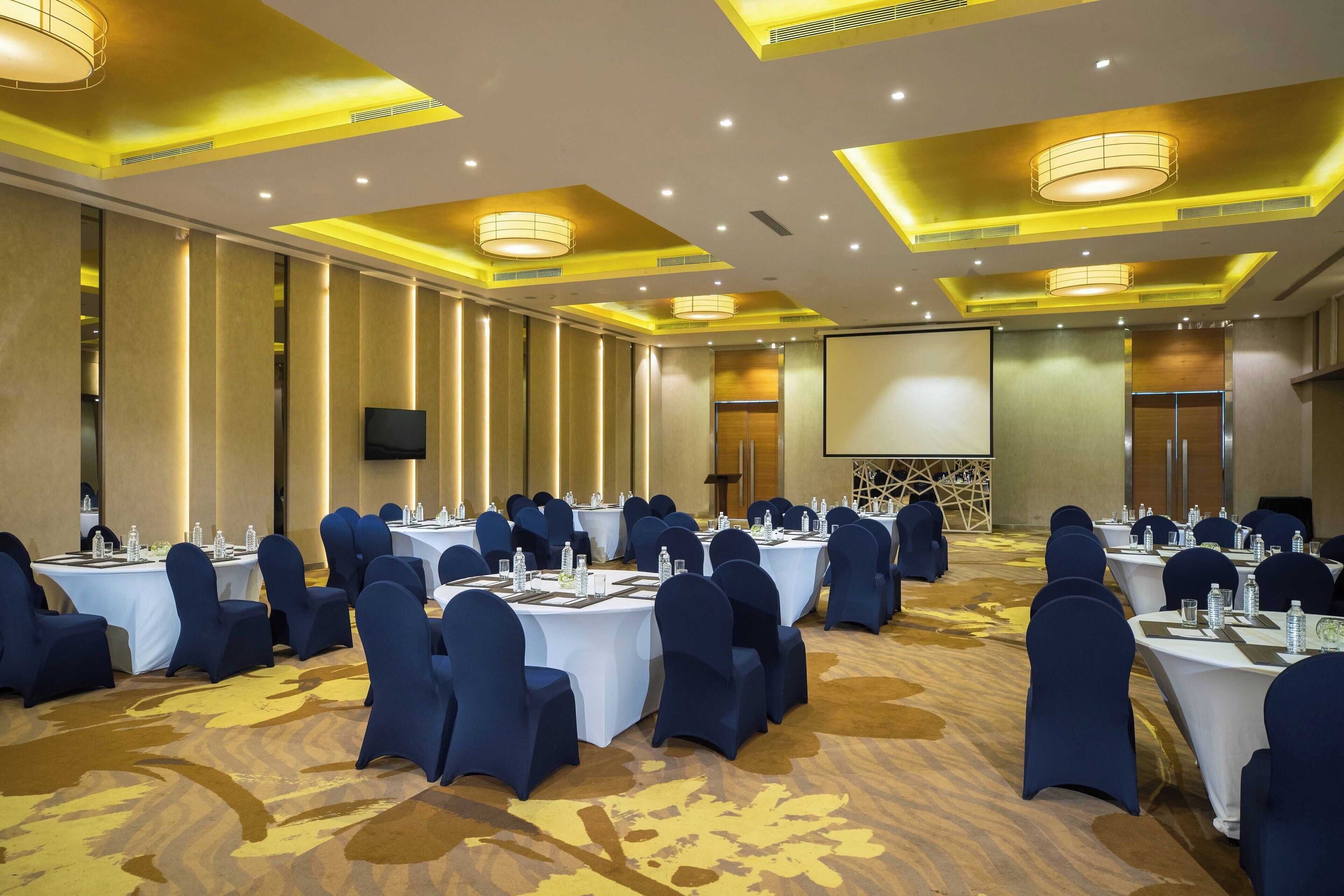 A conference room with round tables, blue chairs, and a large screen.