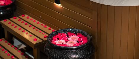 A hot tub with rose petals and a control panel, wooden benches, and a wooden wall.