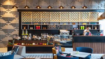 Zona de bar moderna con diversas bebidas y aperitivos, estanterías de madera y una pared con diseño.