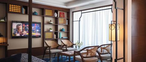 A modern living room with a television, comfortable seating, a bookshelf, and a large window with curtains.