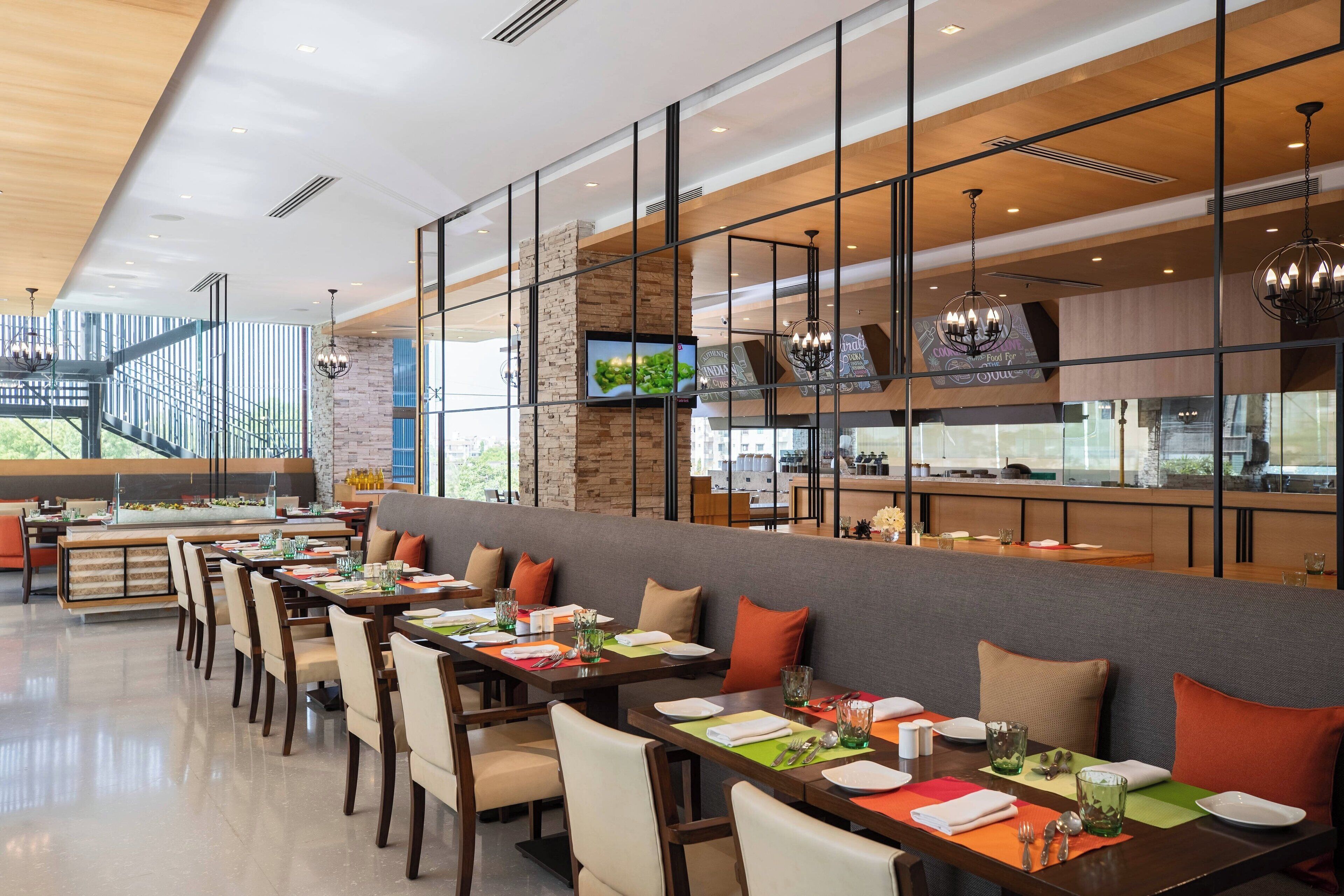 Un restaurante moderno con varias mesas, sillas y una cocina visible a través de un separador de vidrio.