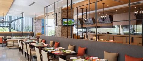 Un restaurant moderne doté de nombreuses tables, de chaises et d’un espace cuisine visible à travers une paroi en verre.