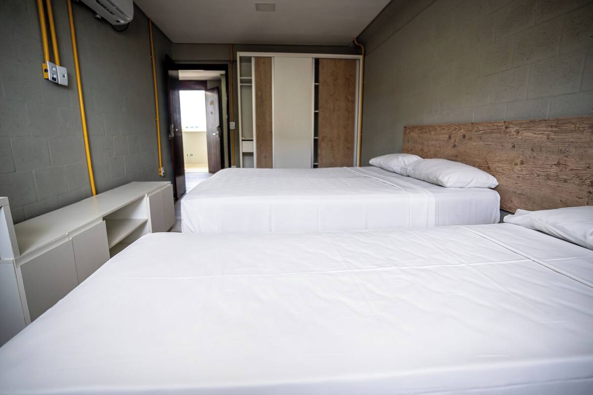 A hotel room with two beds, a wooden headboard, a white bedside table, and a wardrobe with a sliding door.