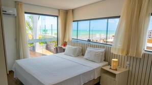 A hotel room with a large bed, a nightstand with a lamp, and a view of the beach. - Bessa Golden Flats (João Pessoa)
