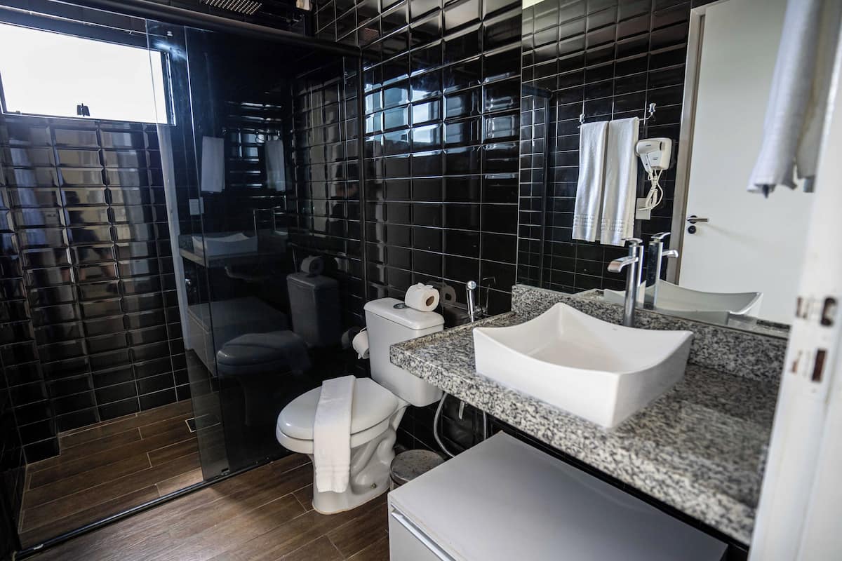 A modern bathroom with a black tiled wall, a white sink, and a toilet.