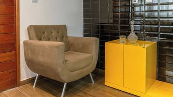Une pièce moderne avec un fauteuil à capitons, un meuble jaune et un mur recouvert de carreaux noirs.
