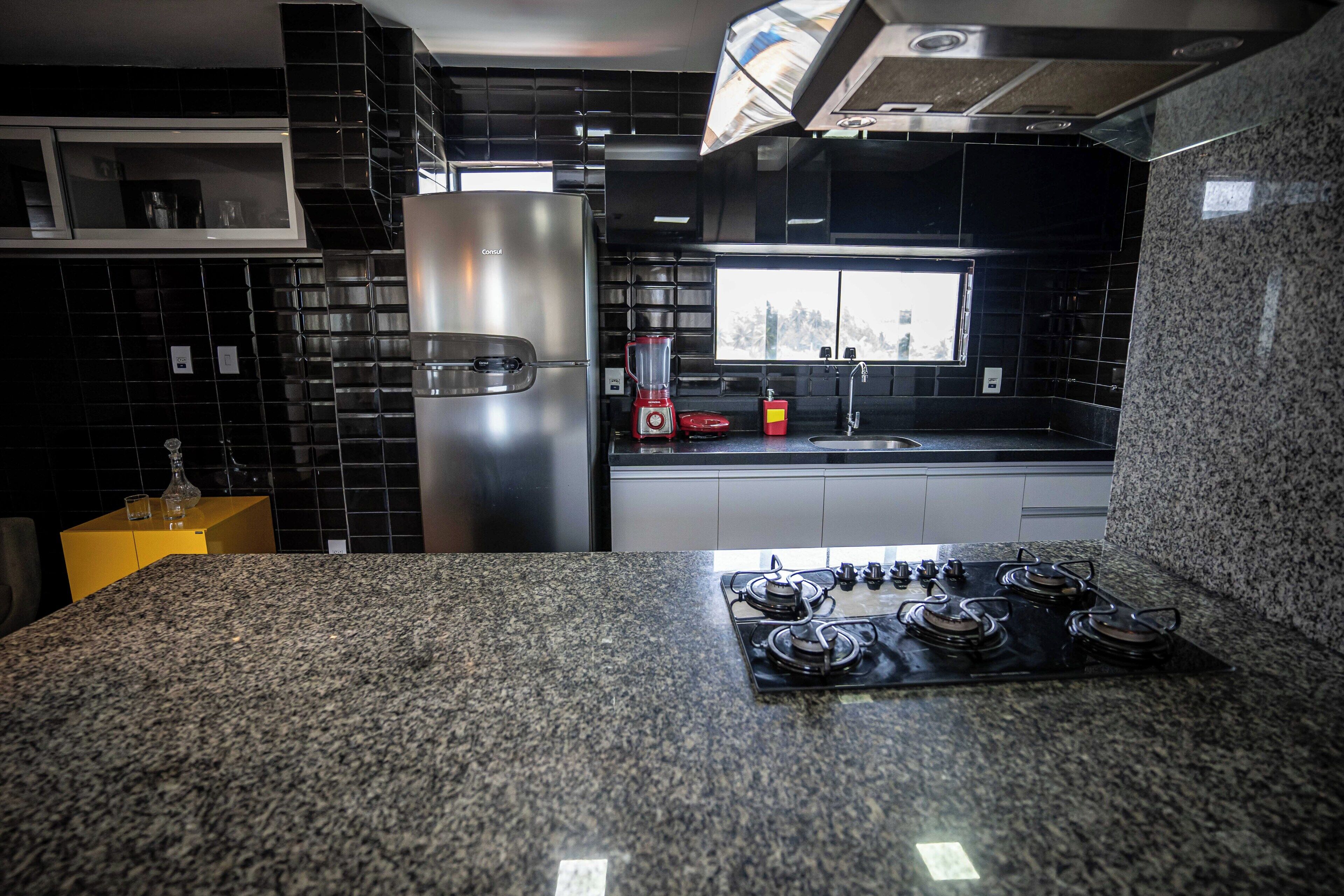 Cozinha moderna com bancadas de granito, eletrodomésticos de aço inoxidável e painel de azulejos preto.