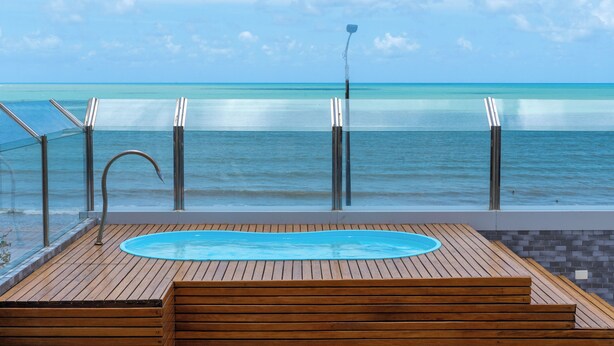 A wooden deck with a pool, overlooking a beach with clear turquoise water and a calm sea. - Bessa Golden Flats (João Pessoa)