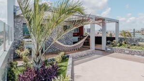 A modern outdoor patio with a hammock, palm tree, and various plants. - Bessa Golden Flats (João Pessoa)