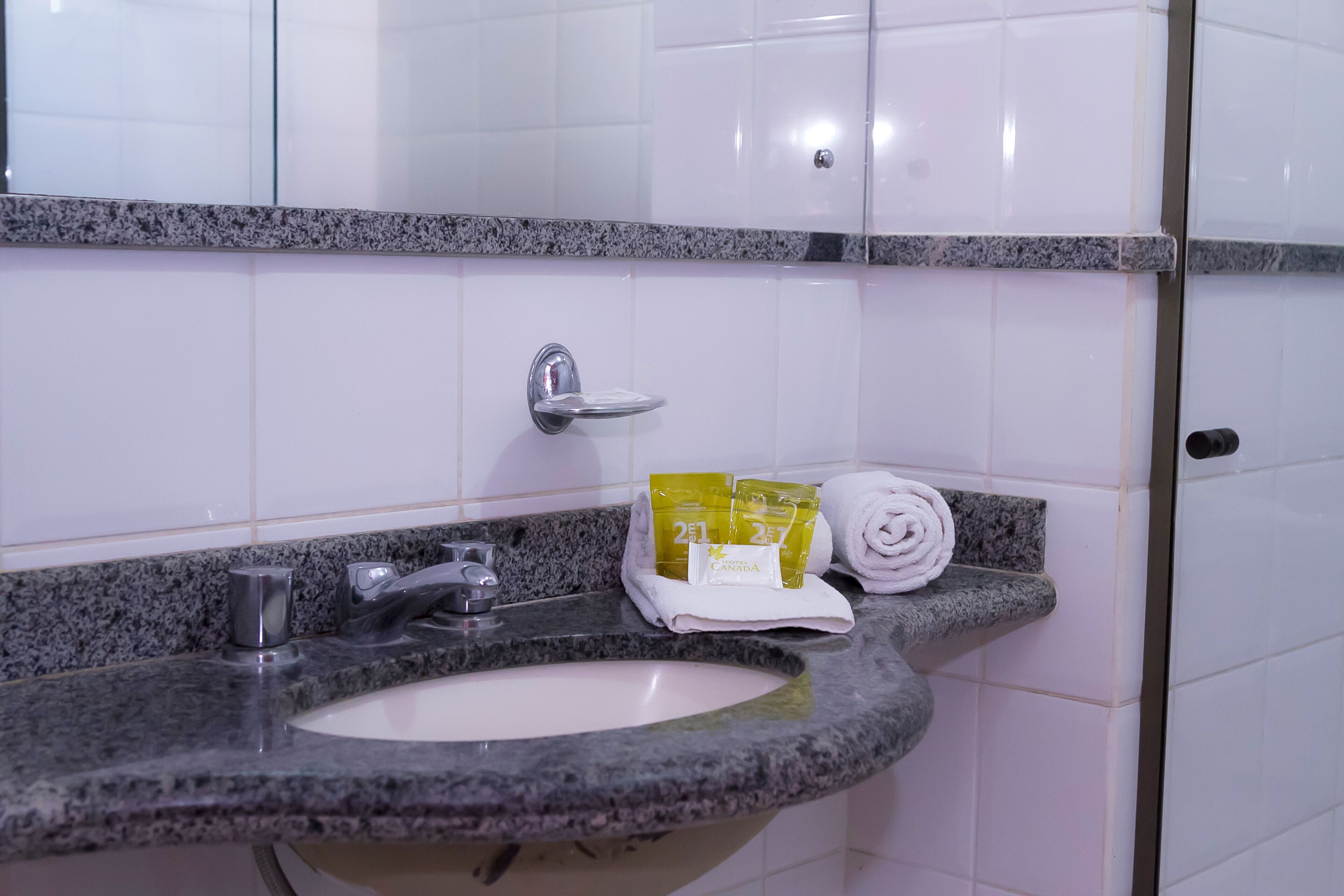 A bathroom with a granite countertop sink, a mirror, and a towel rack with towels and toiletries.