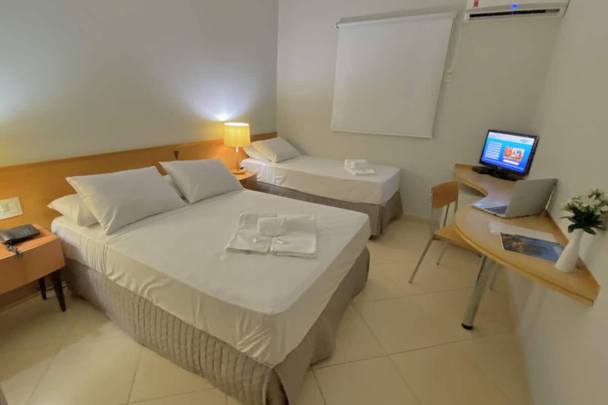 Habitación de hotel con dos camas, un escritorio con computadora, una silla, una lámpara y televisor montado en la pared.