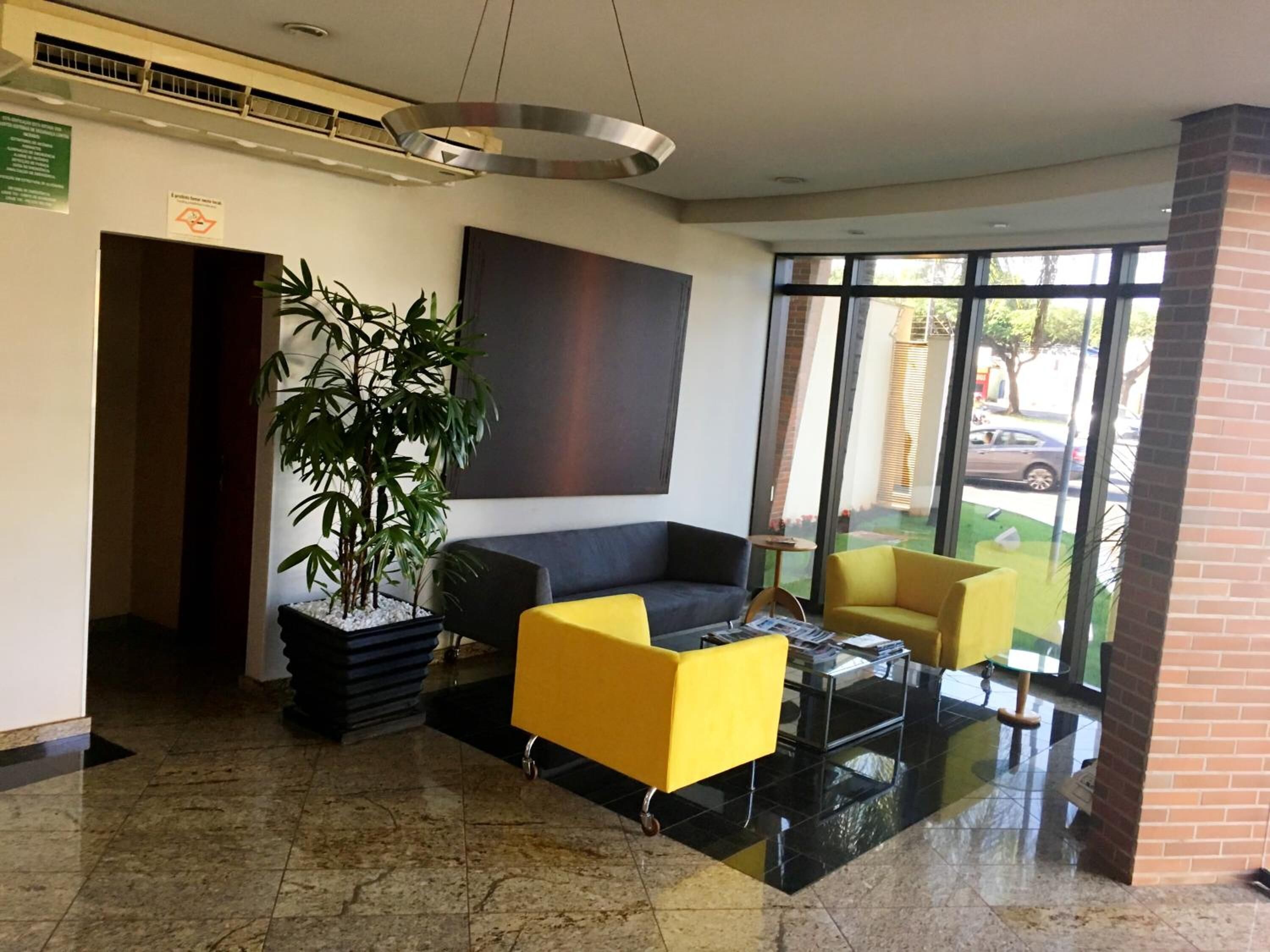 A lobby with a black sofa, a yellow armchair, a large potted plant, and a glass coffee table.
