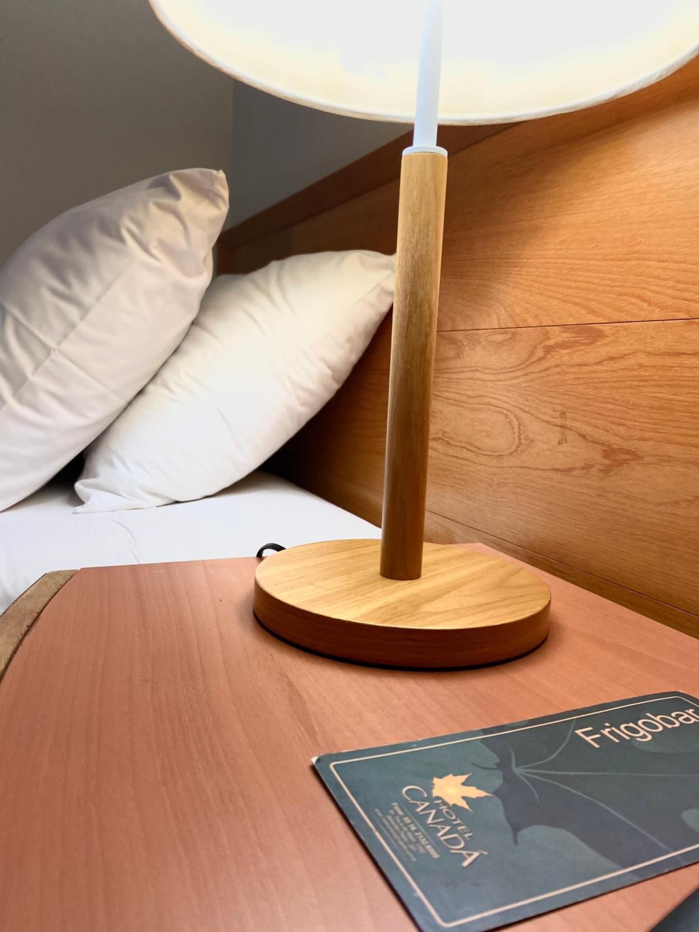 Ein Nachttisch aus Holz mit einer Lampe, einem Kopfkissen und einer Hotelleiterkarte.