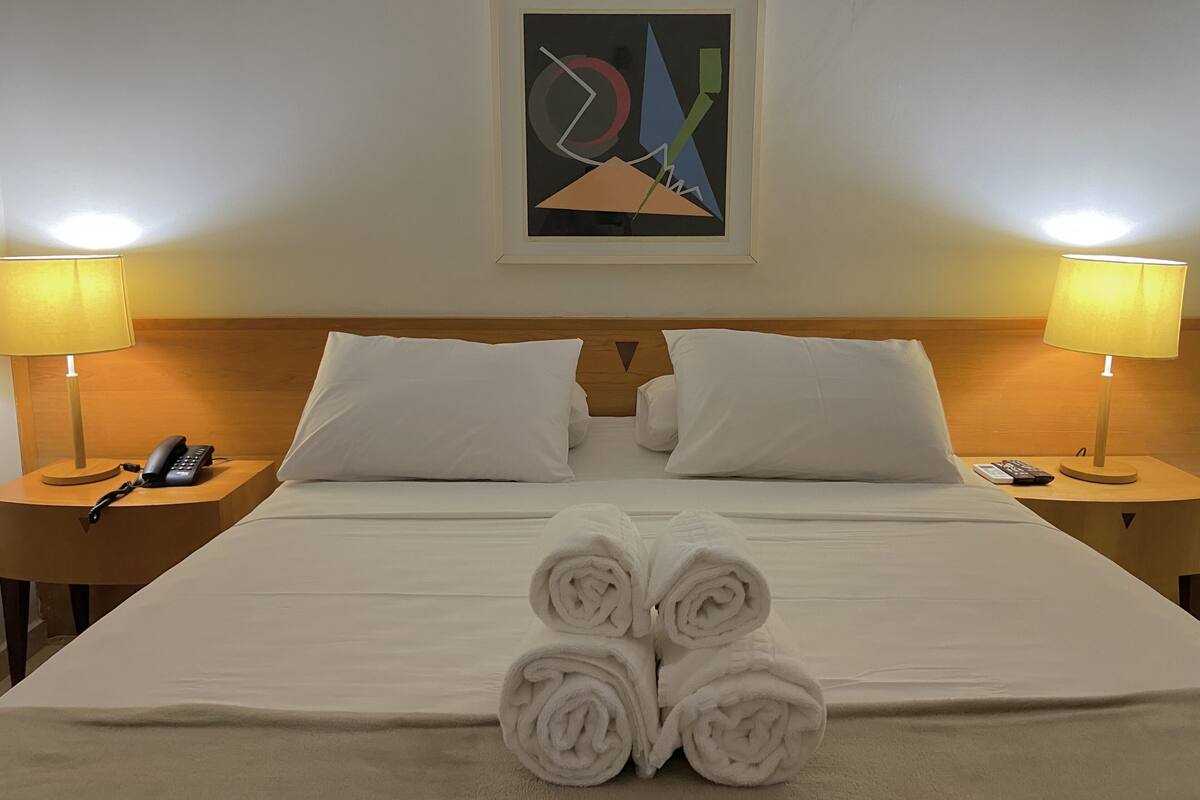 Una habitación de hotel con una cama bien hecha, dos lámparas de noche, un teléfono y un cuadro en la pared.