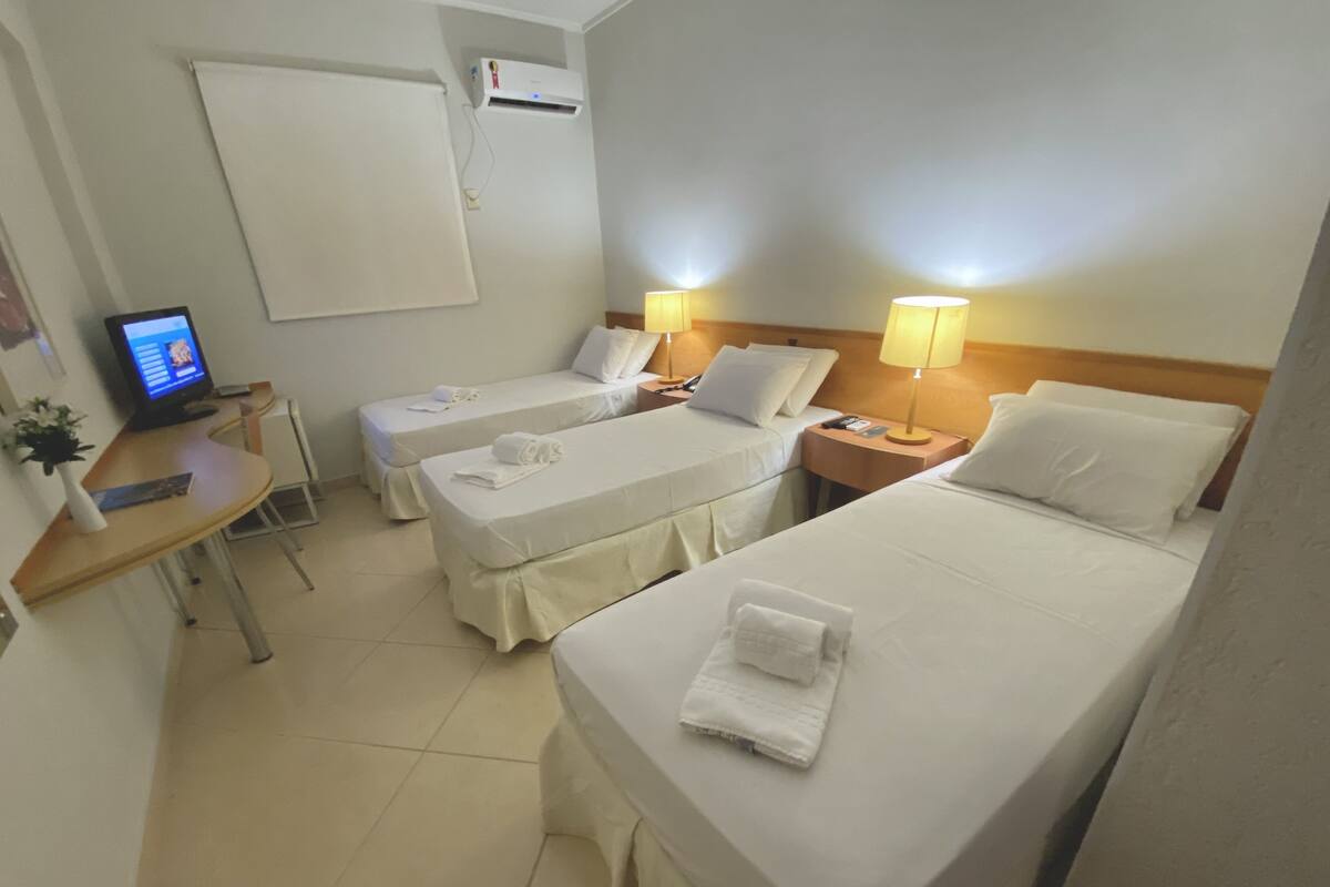 Habitación de hotel con dos camas individuales, un escritorio con computadora, una silla y aire acondicionado de pared.
