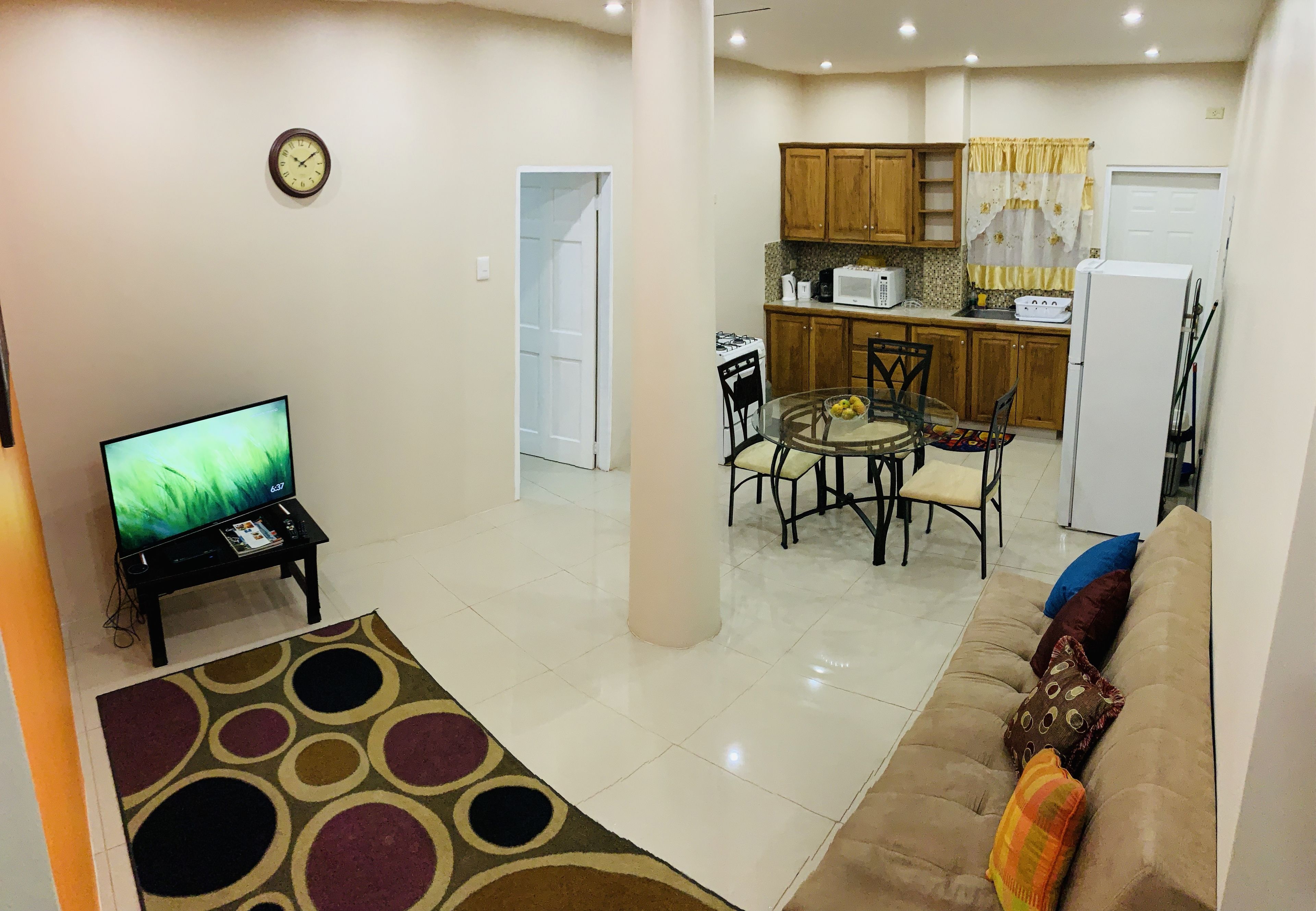 A living room with a TV, a sofa, a coffee table, and a dining area with chairs and a table.