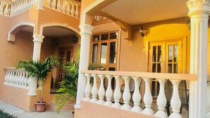 A multi-story building with a balcony, white balustrades, and potted plants. - Robbie's Place Tobago (Black Rock)