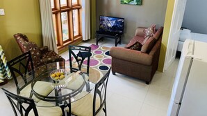A living room with a sofa, TV, and a dining table with chairs. - Robbie's Place Tobago (Black Rock)