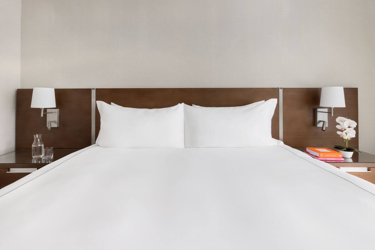 A neatly made bed with white linens, two bedside tables with lamps, a small vase, and a few books.