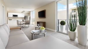 A modern living room with a sofa, a coffee table with a vase, and a dining area with chairs and a table. - The Altair Bay Harbor Hotel (Bay Harbor Islands)