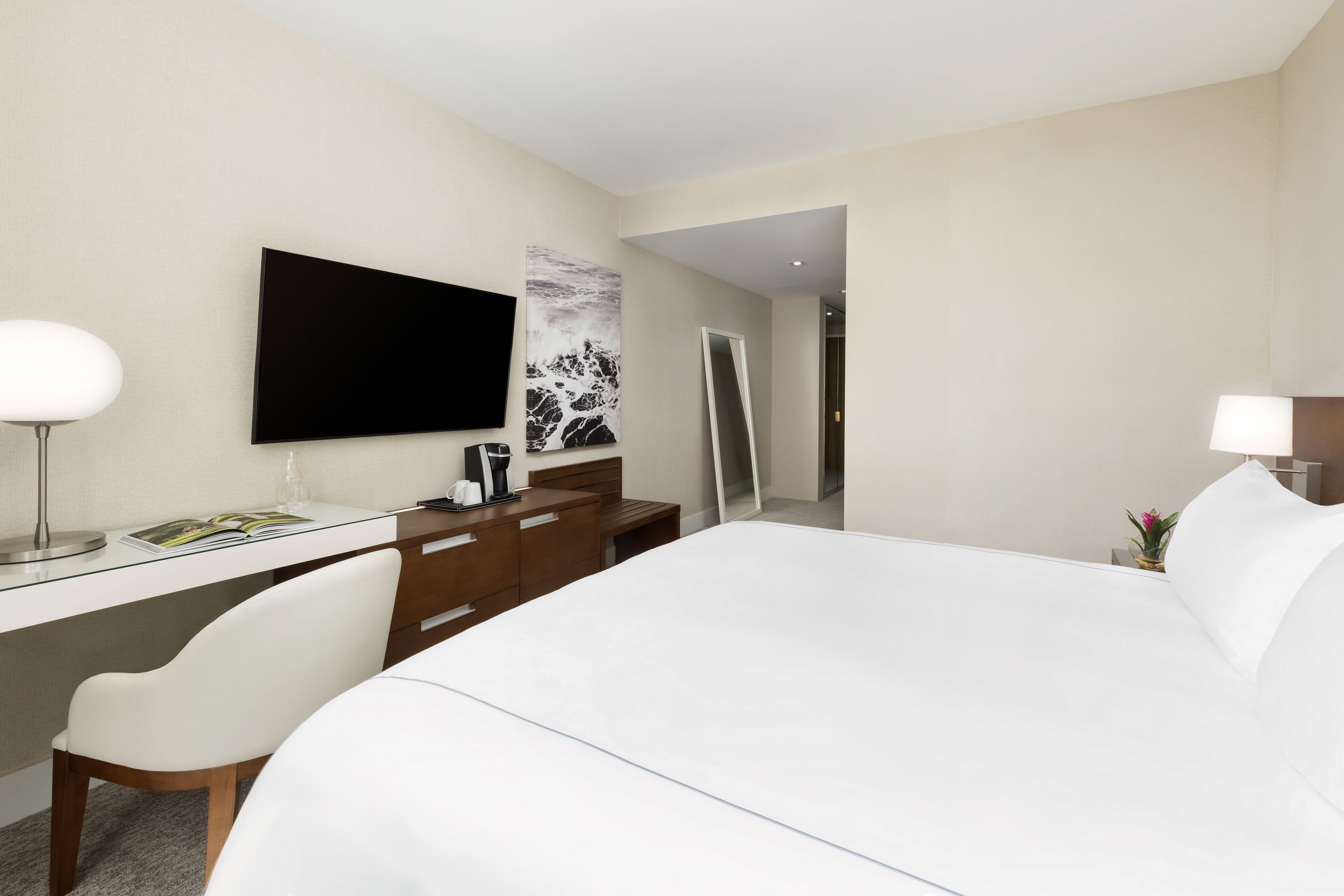 A hotel room with a bed, a desk, a chair, a TV, and a mirror.