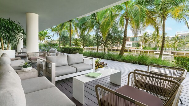 A modern outdoor seating area with a sofa, chairs, and a table, surrounded by lush greenery and palm trees. - The Altair Bay Harbor Hotel (Bay Harbor Islands)