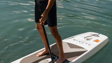 Un homme se tient debout sur une planche à pagaie dans l’eau, une pagaie à la main.
