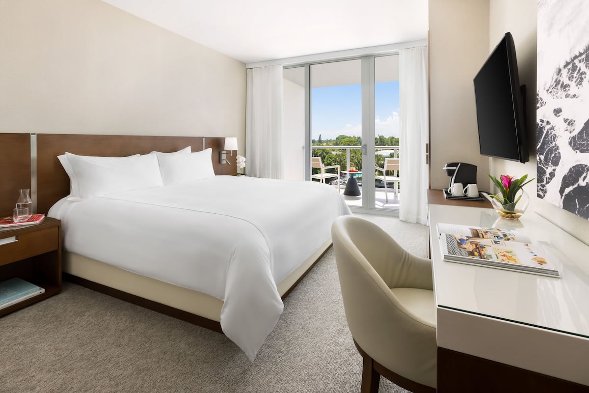 A hotel room with a large bed, a desk with a chair, a TV, and a view of the outdoors.