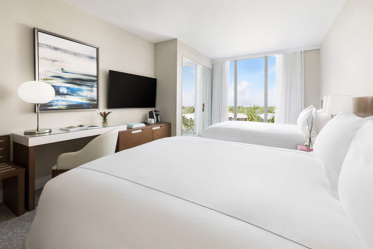 A hotel room with a large bed, a desk, a chair, a TV, and a window with a view of greenery.