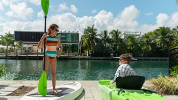 Ein Poolbereich mit Stand-Up-Paddleboard und Kajak, im Hintergrund ein modernes Gebäude und Palmen.