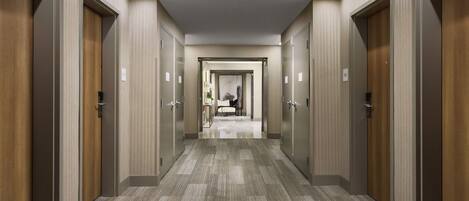 Un couloir d’hôtel avec de nombreuses portes, un sol recouvert de moquette et un luminaire au plafond.