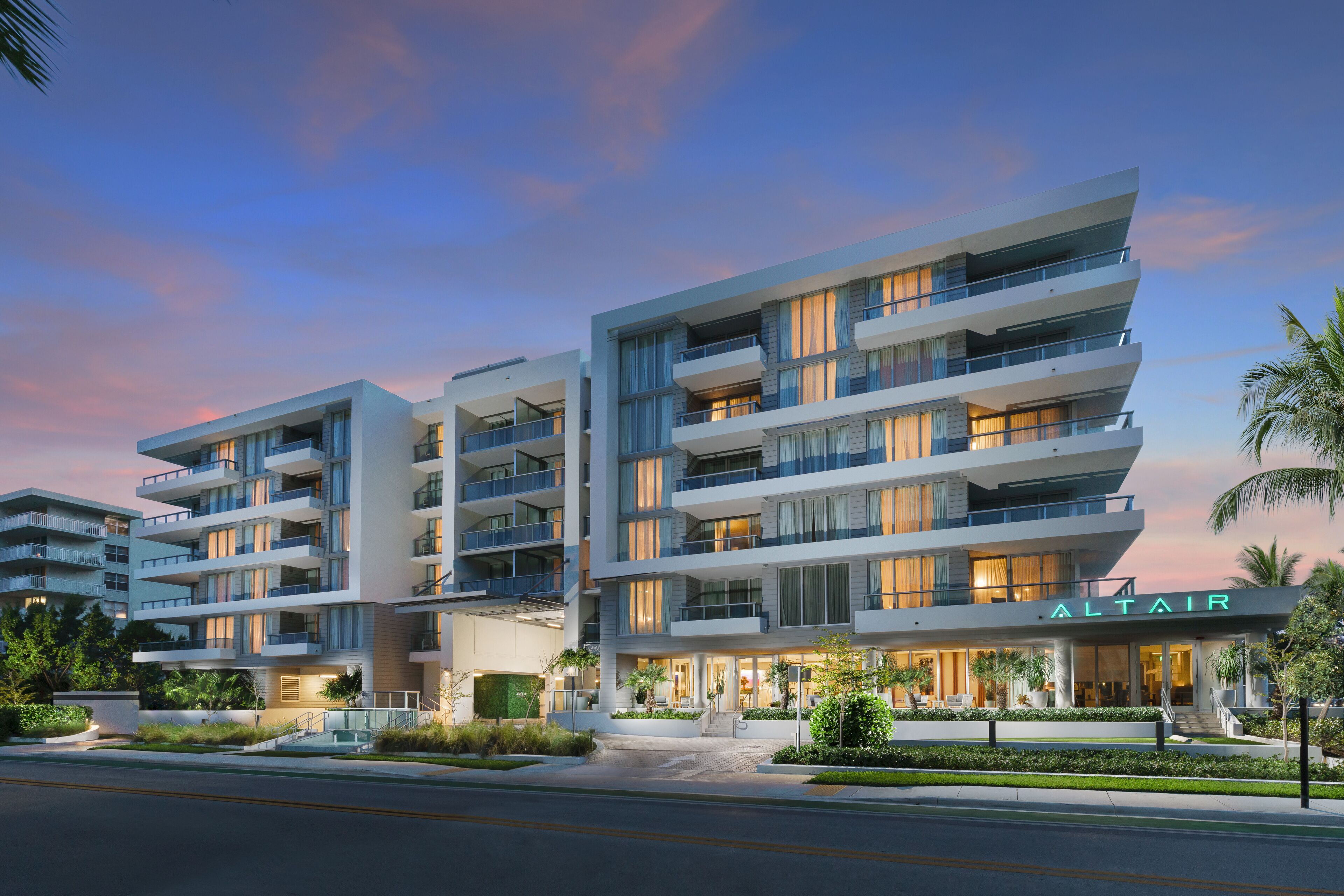 A multi-story hotel with balconies, a well-lit entrance, and a landscaped outdoor area.