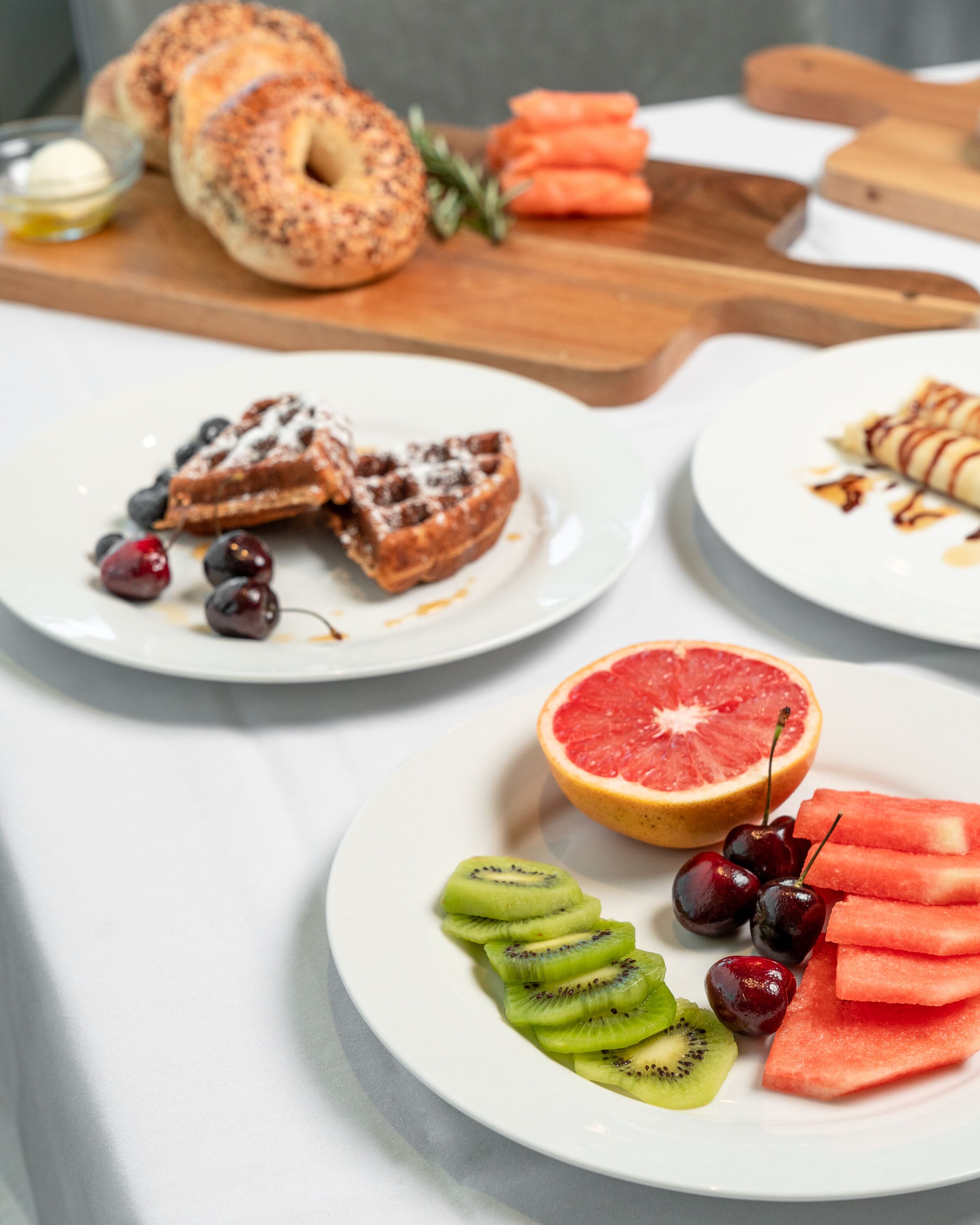 A breakfast table with various food items including bagels, waffles, and fresh fruit.
