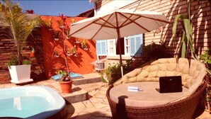 Un espace piscine agrémenté d’un fauteuil en osier et d’un parasol, entouré de plantes en pot et d’un mur en briques.