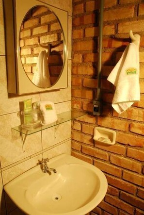 Un baño con lavamanos, espejo y perchero frente a una pared de ladrillo.