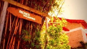 Une enseigne en bois portant l’inscription « RECANTO DOS BANHUS », placée dans un cadre rustique agrémenté de bambous et de verdure.